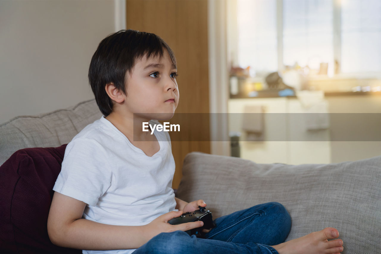 Boy playing game while sitting on sofa at home