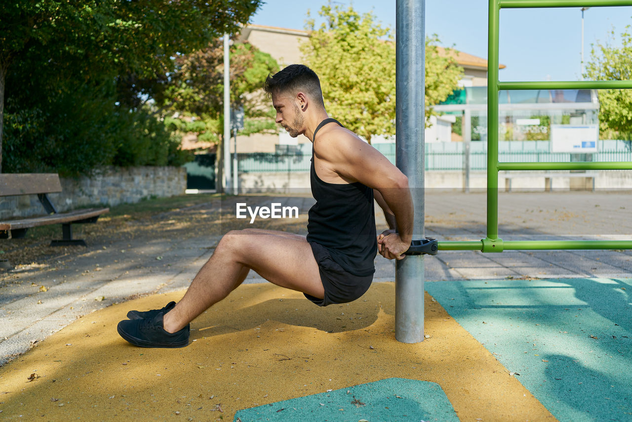 Side view of a man practicing calisthenics in a park on a sunny day
