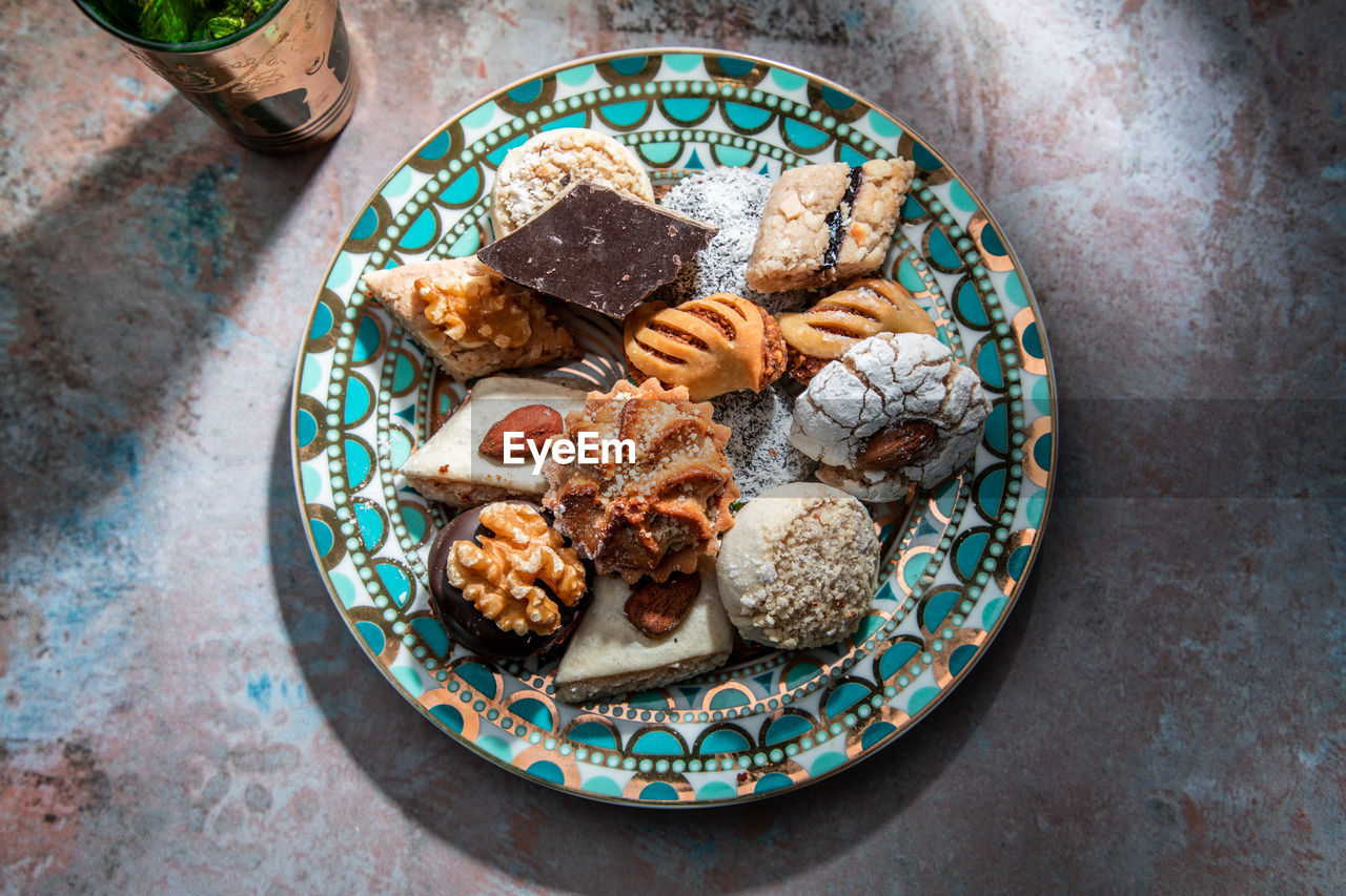 From above of baklava and biscuits with moroccan peppermint tea near knife and fork placed on table decorated with mint leaves