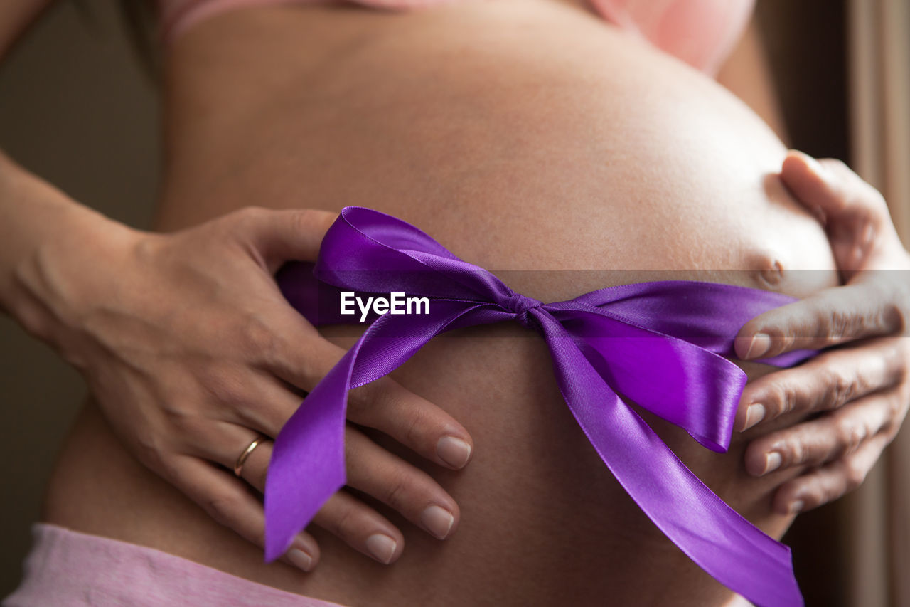 Midsection of pregnant woman with purple ribbon tied on stomach