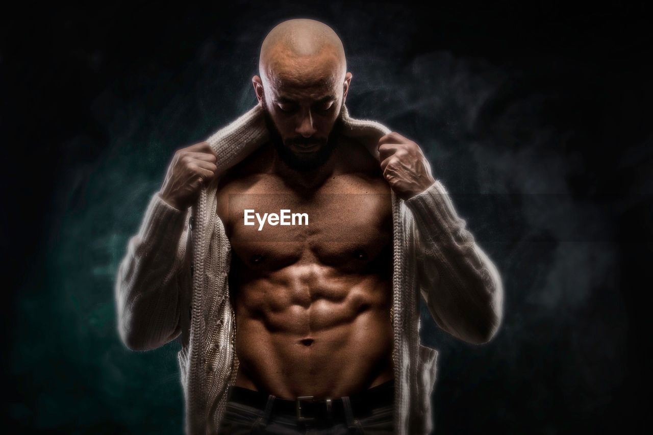 Bald muscular man standing against black background