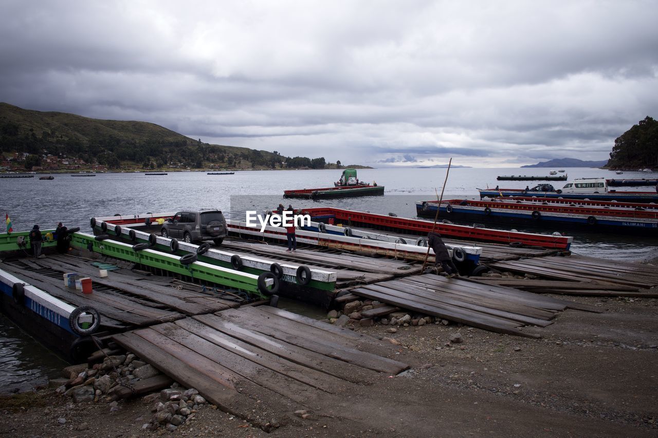 water, transportation, sky, sea, cloud, nautical vessel, coast, mode of transportation, vehicle, boat, nature, land, beach, transport, boating, shore, harbor, environment, overcast, no people, travel destinations, scenics - nature, moored, watercraft, pier, architecture, day, landscape, travel, outdoors, tranquility, bay, dock, beauty in nature, coastline, ship, holiday, tranquil scene, tourism, body of water, mountain, non-urban scene, waterway, dramatic sky, wood, vacation, trip, fishing