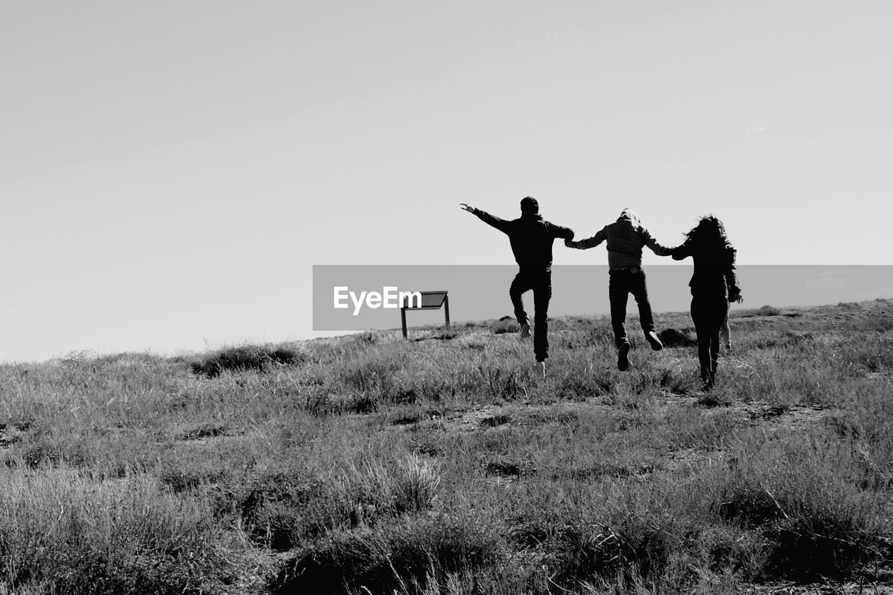 Friends jumping on field against clear sky