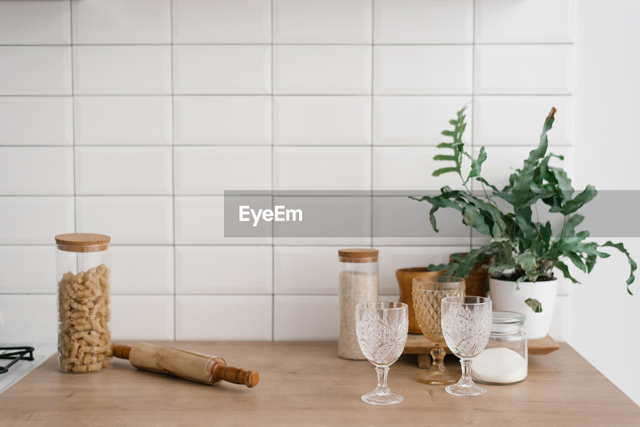 A glass jar with pasta, glasses, a rolling pin and a houseplant stand in the bright kitchen