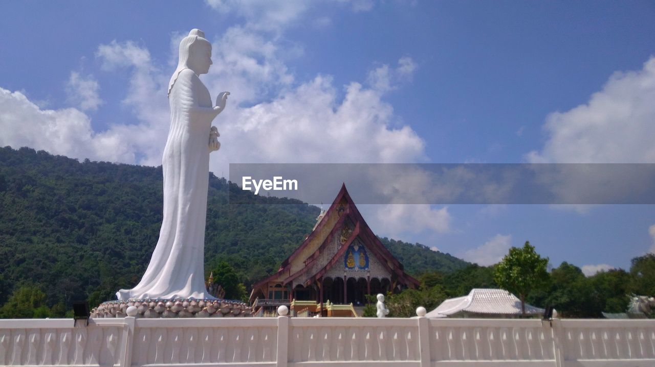 STATUE BY TREES AND BUILDING AGAINST SKY