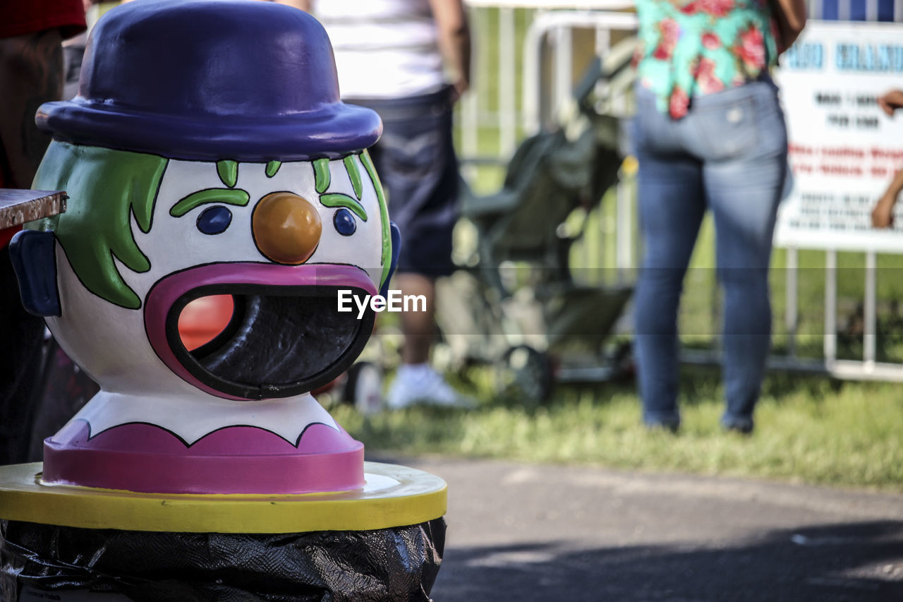 Close-up of clown garbage can with people standing in background