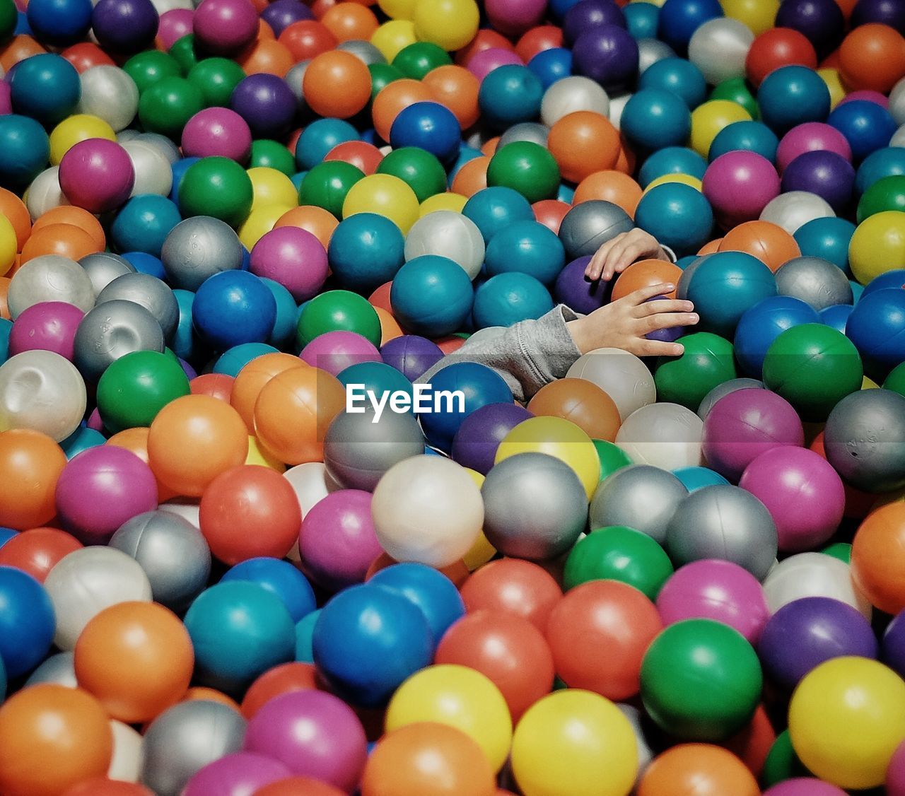 Cropped hands of child amidst colorful ball pool