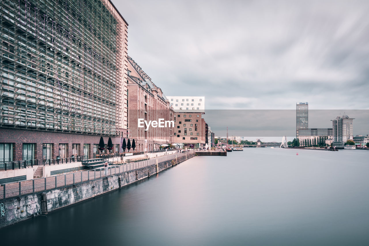 River by buildings against cloudy sky