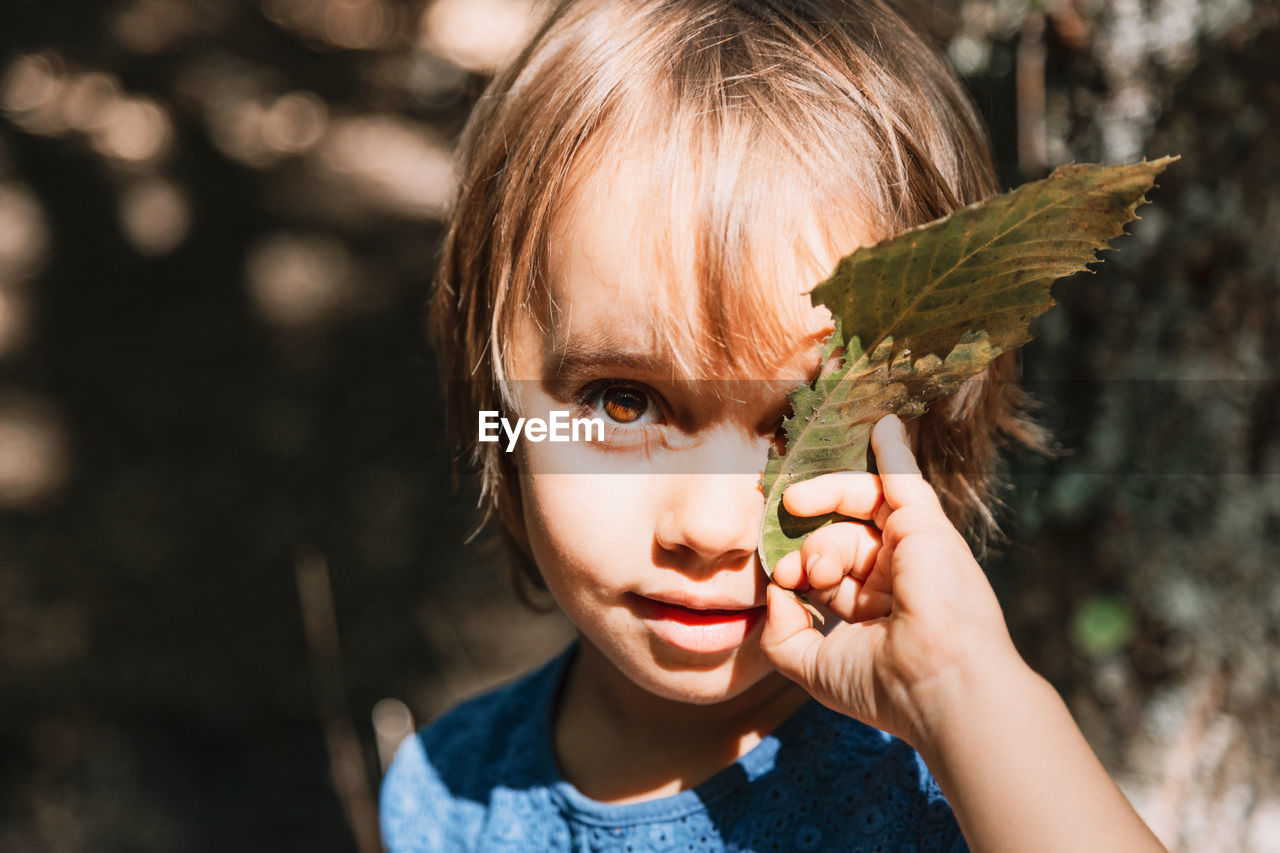 Close-up portrait of girl holding leaf in forest