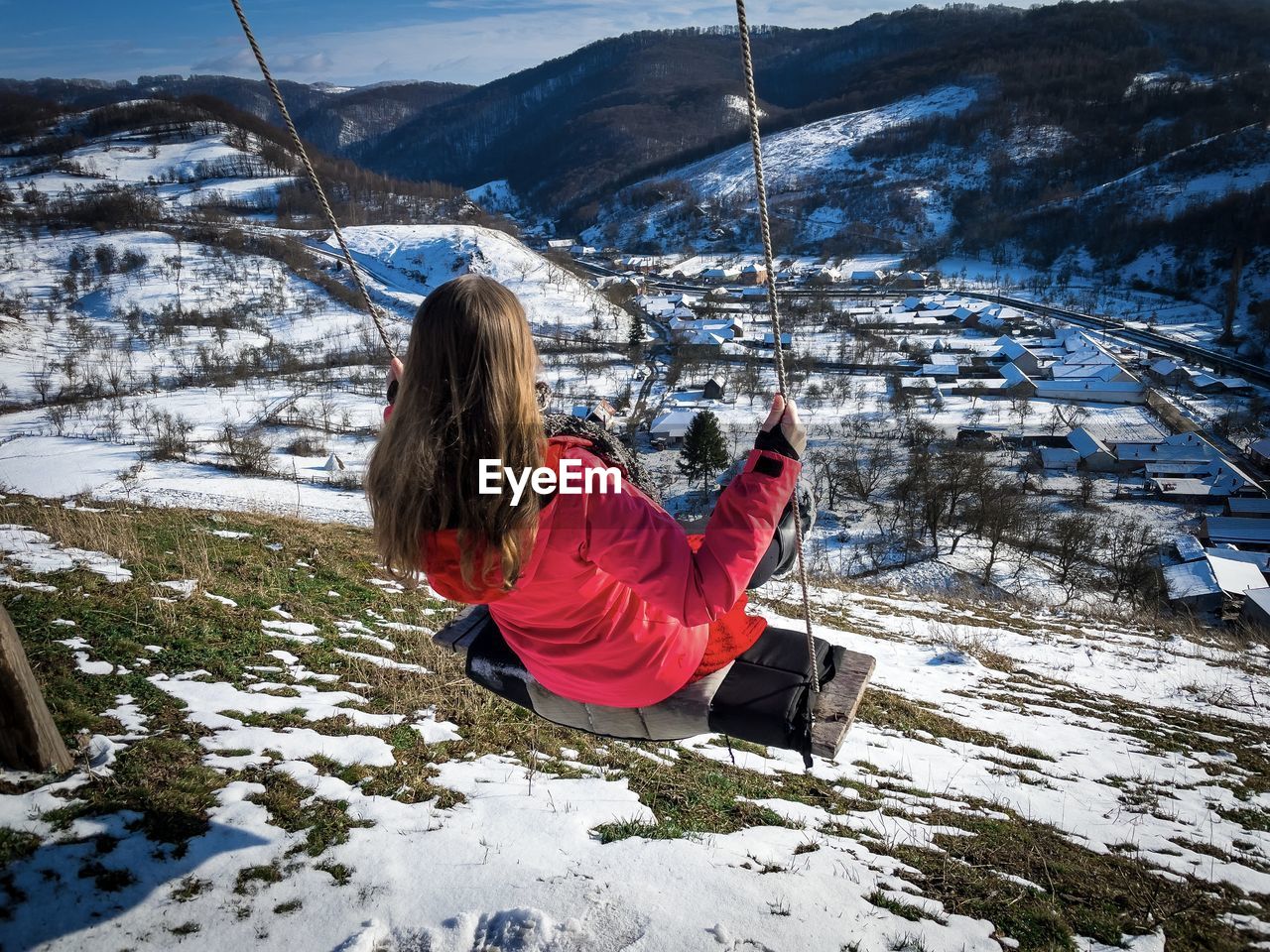 Woman in a rope swing on top of the mountains during winter with a beautiful panoramic view