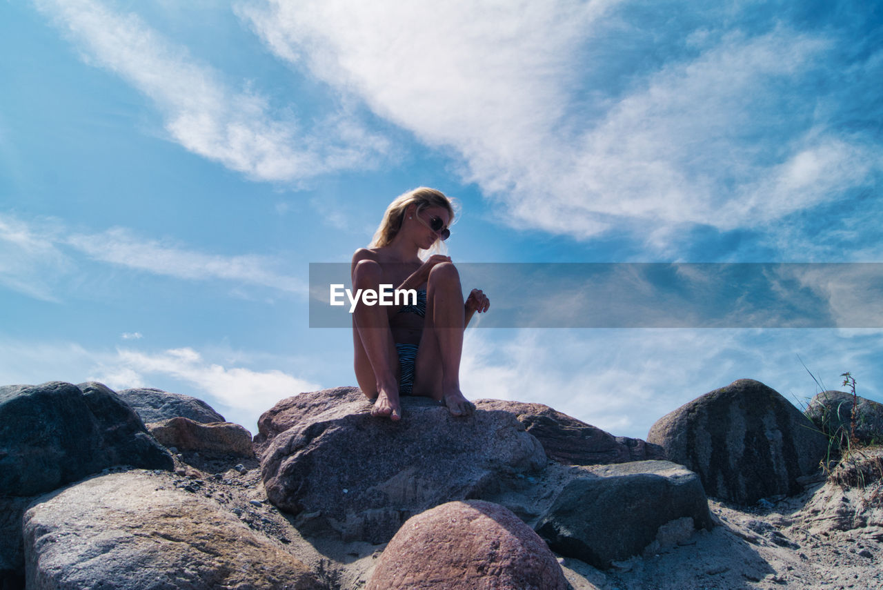 Low angle view of woman in bikini sitting on rock at beach against sky, timmendorfer strand 