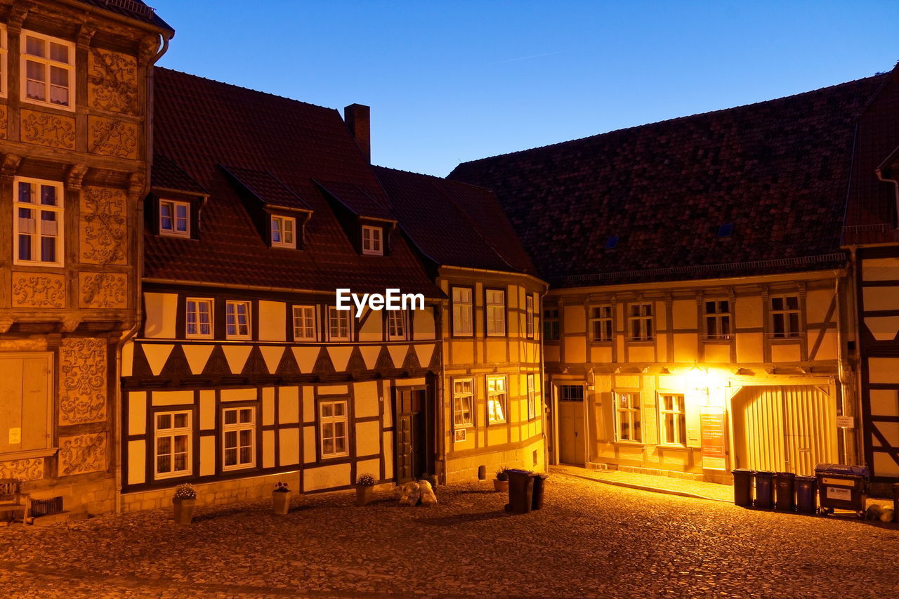 Illuminated street amidst buildings against sky at dusk