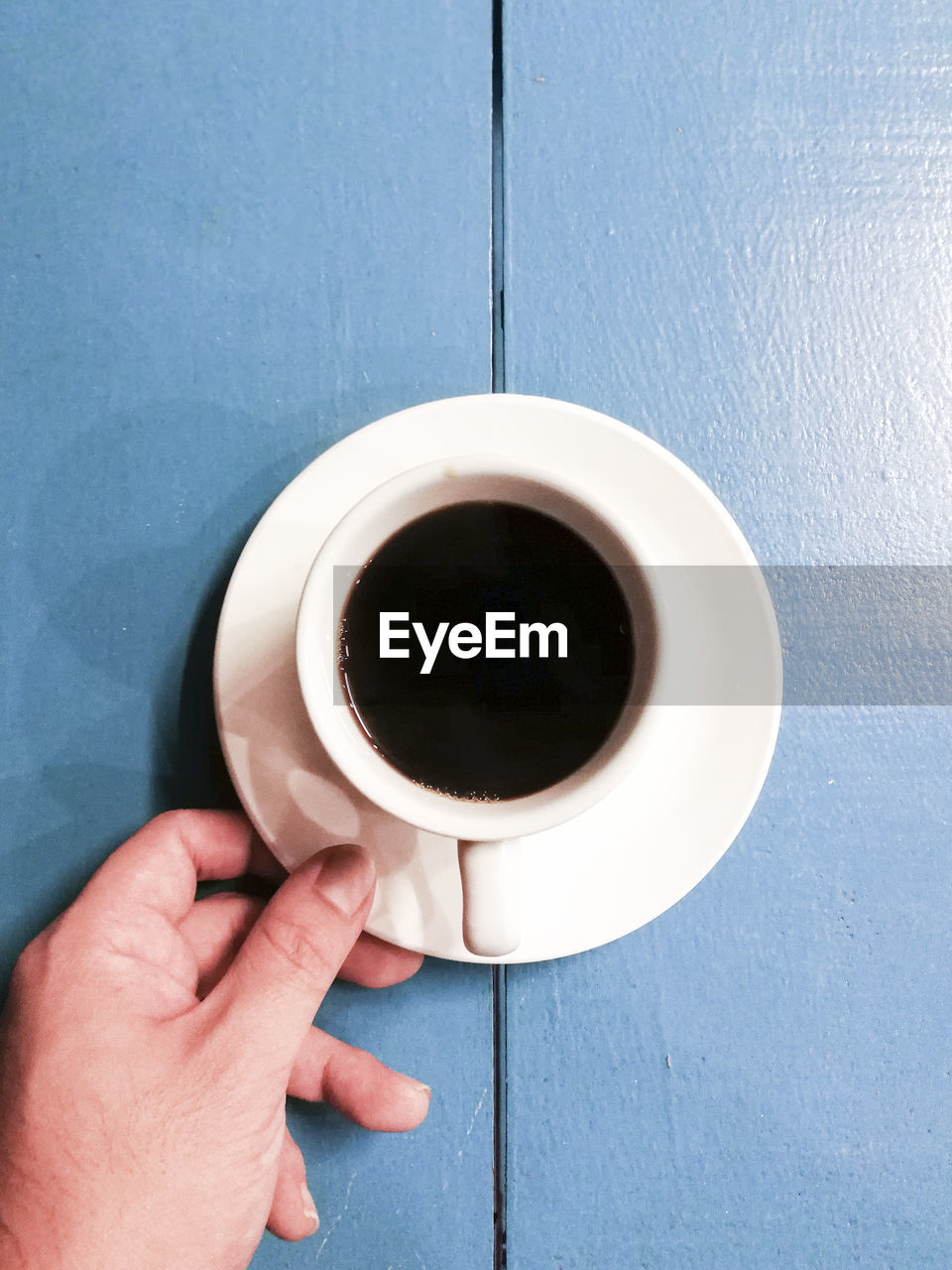 Close-up of hand holding coffee cup on table