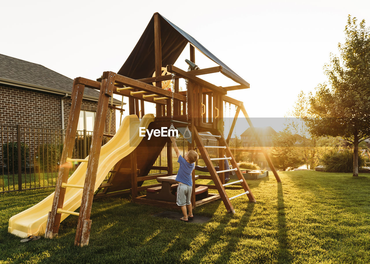 Boy playing with jungle gym in backyard during sunset