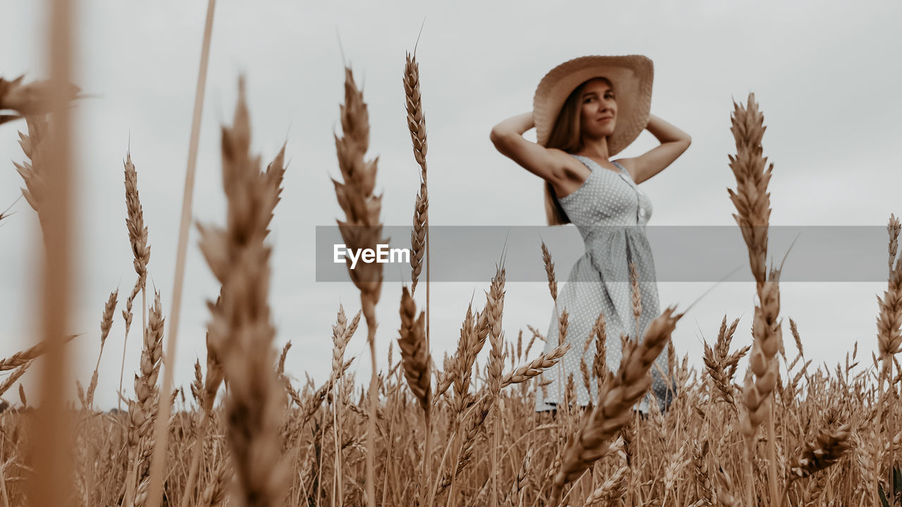 Young woman with arms raised on field against sky