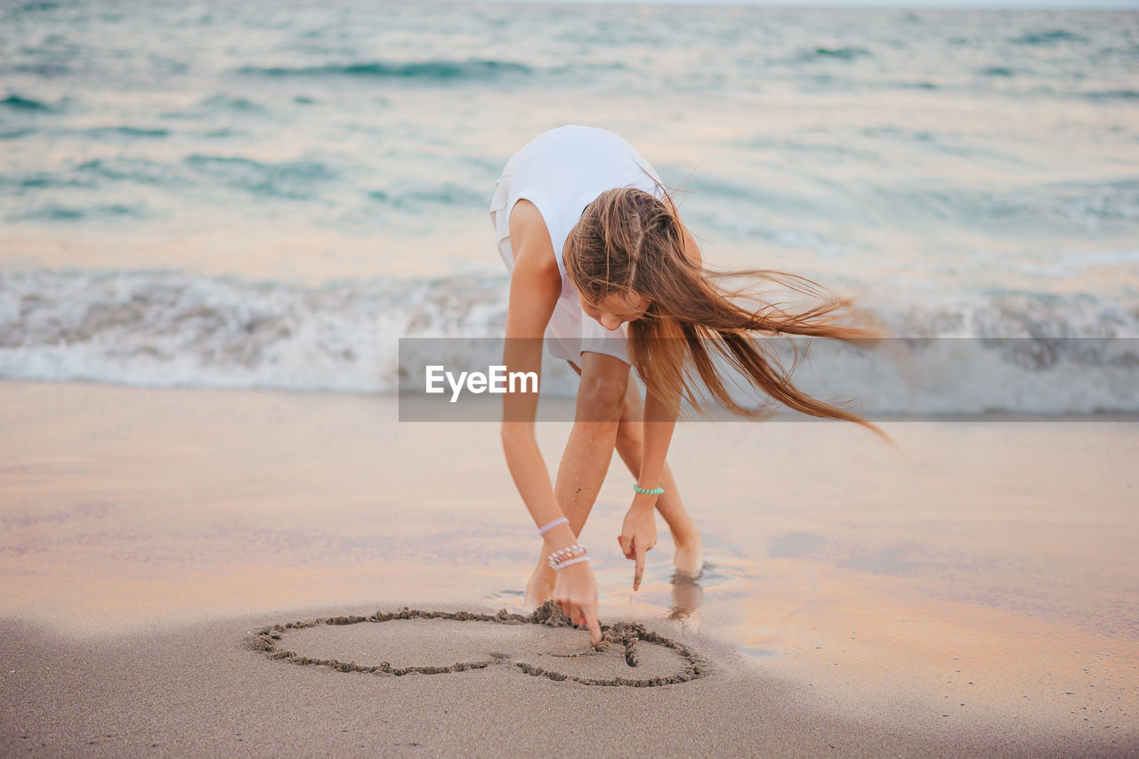 full length of young woman standing at beach against sky during sunset