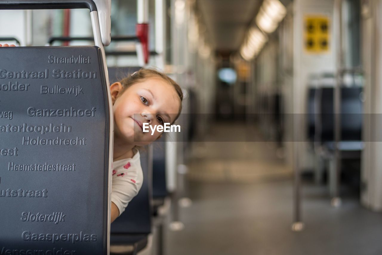 Girl peeking out from behind a seat on empty metro car