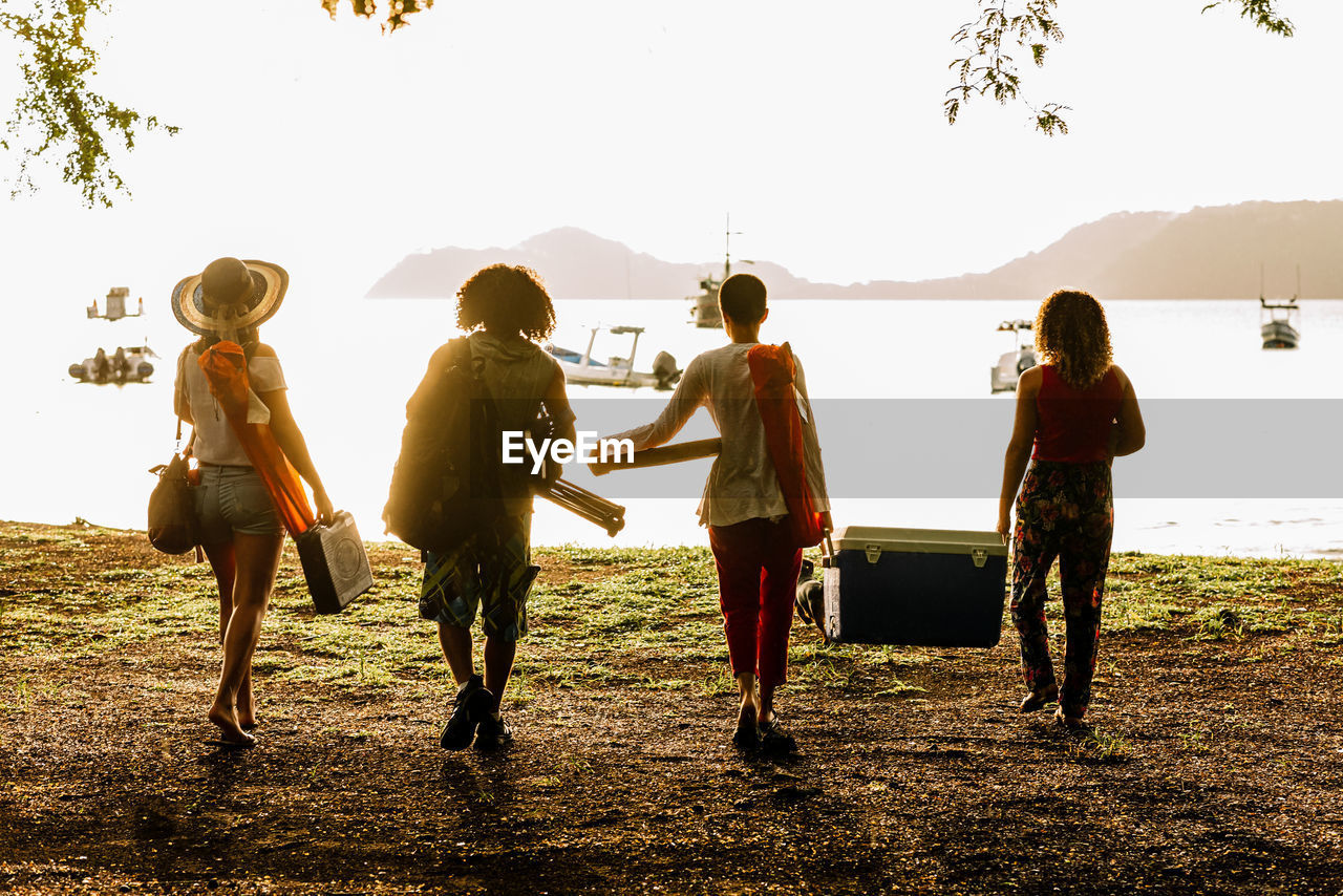 Back view full body of young friends carrying food and supplies for summer picnic on beach of costa rica