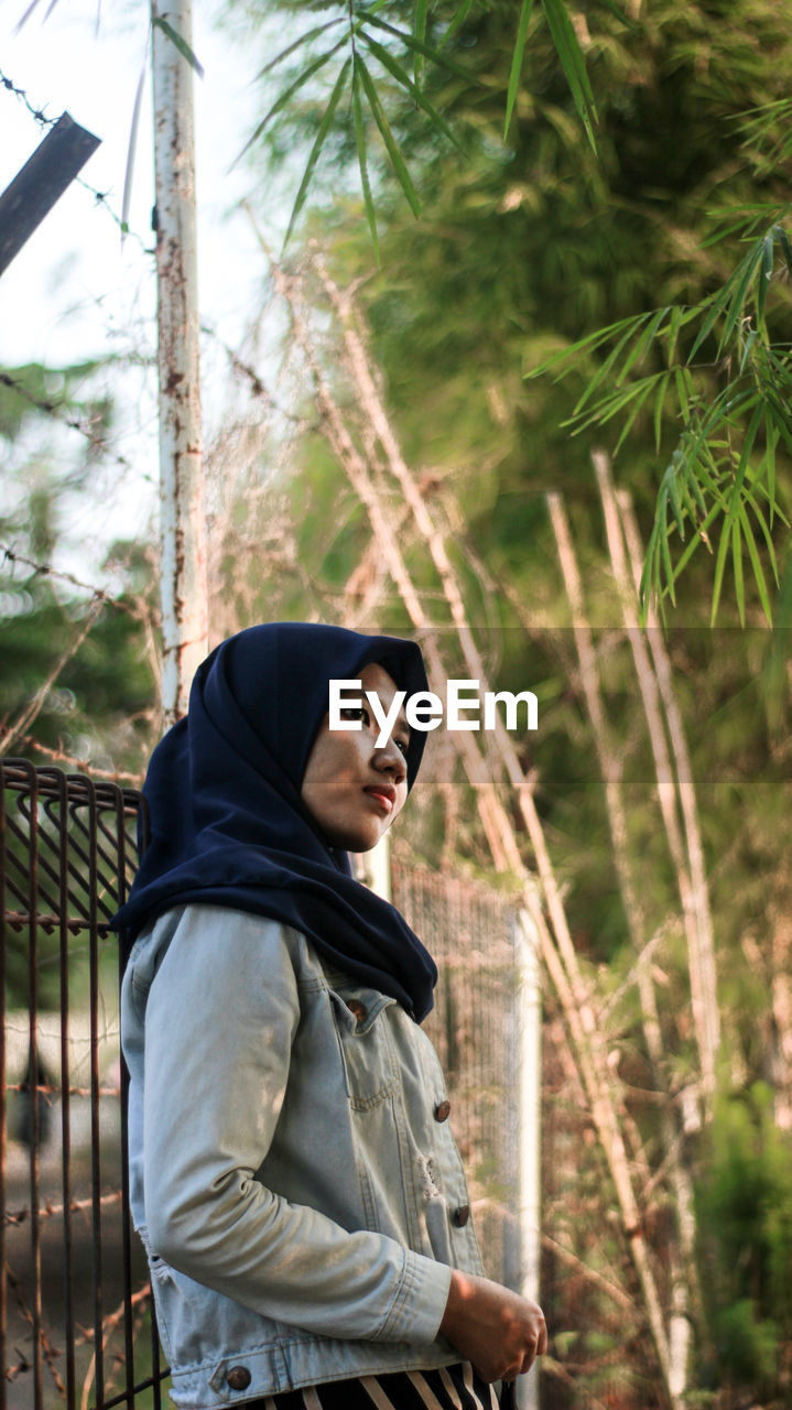 Woman looking away while standing against trees