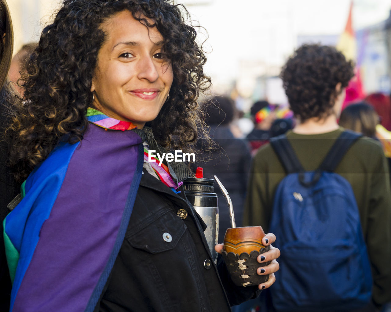 Woman looking at camera while holding a mate with a rainbow flag in an lgbtq pride march.