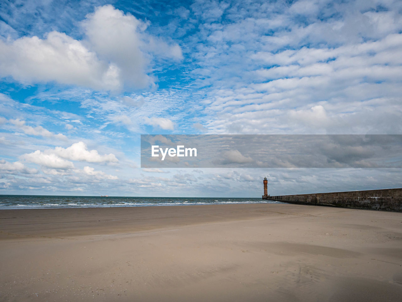 Pier at the beach leading towards lighthouse in the distance