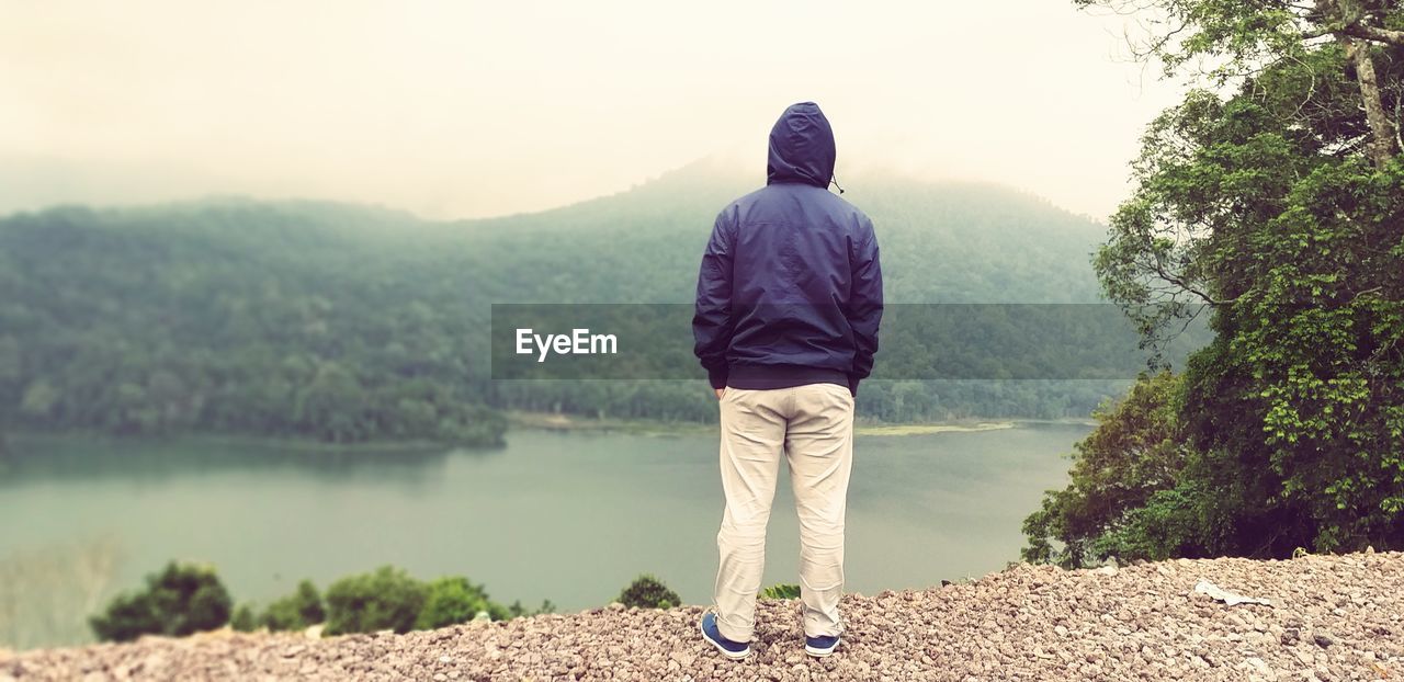 REAR VIEW OF MAN LOOKING AT WATERFALL