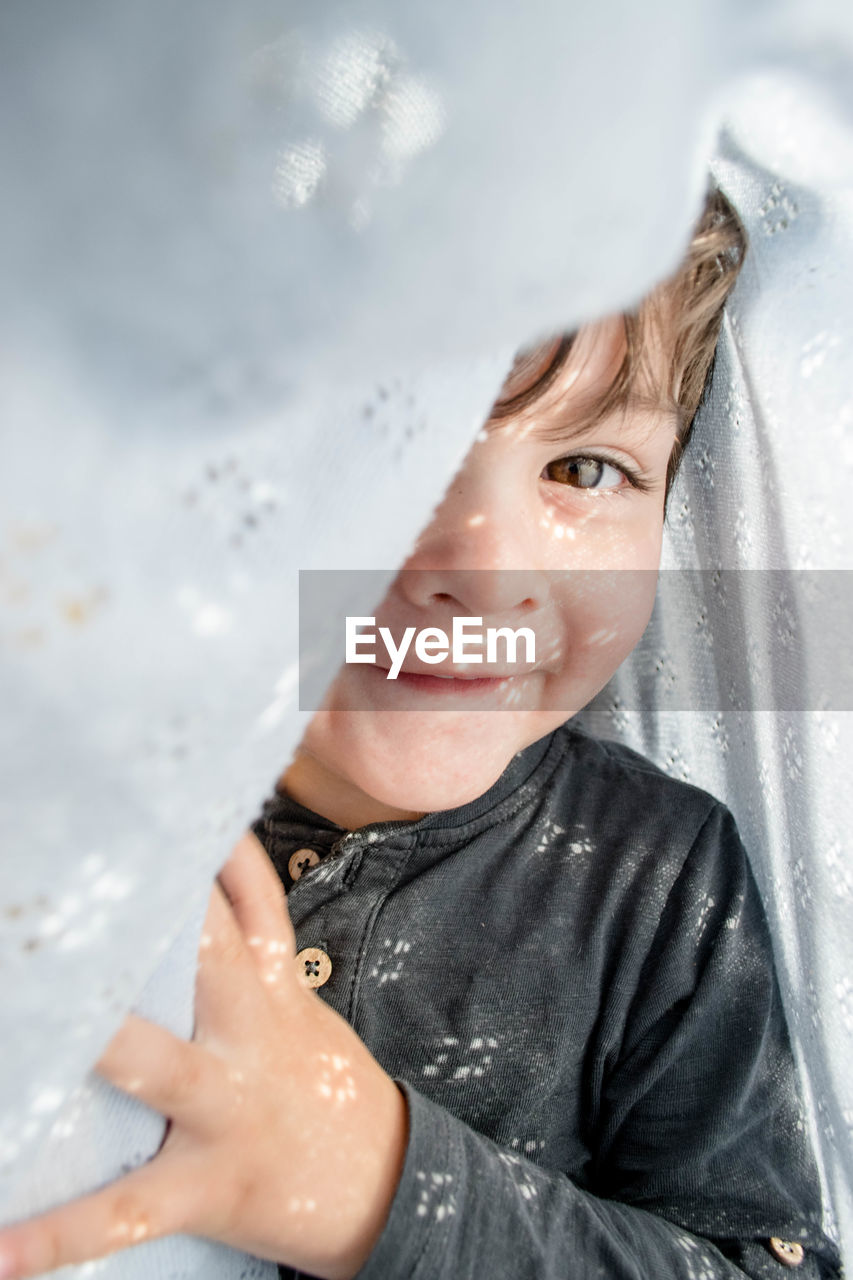 Portrait of boy smiling amidst white curtain