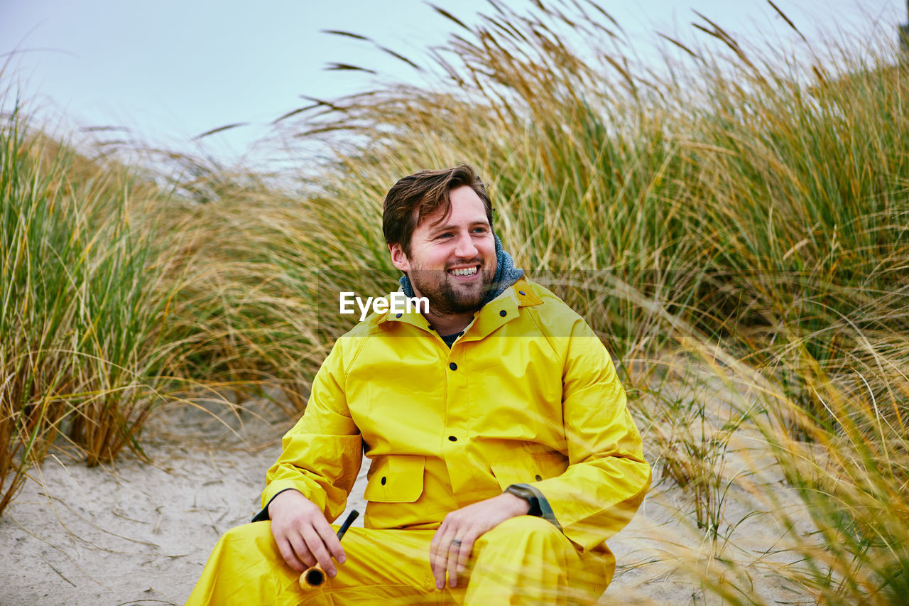 Smiling man sitting at beach against sky