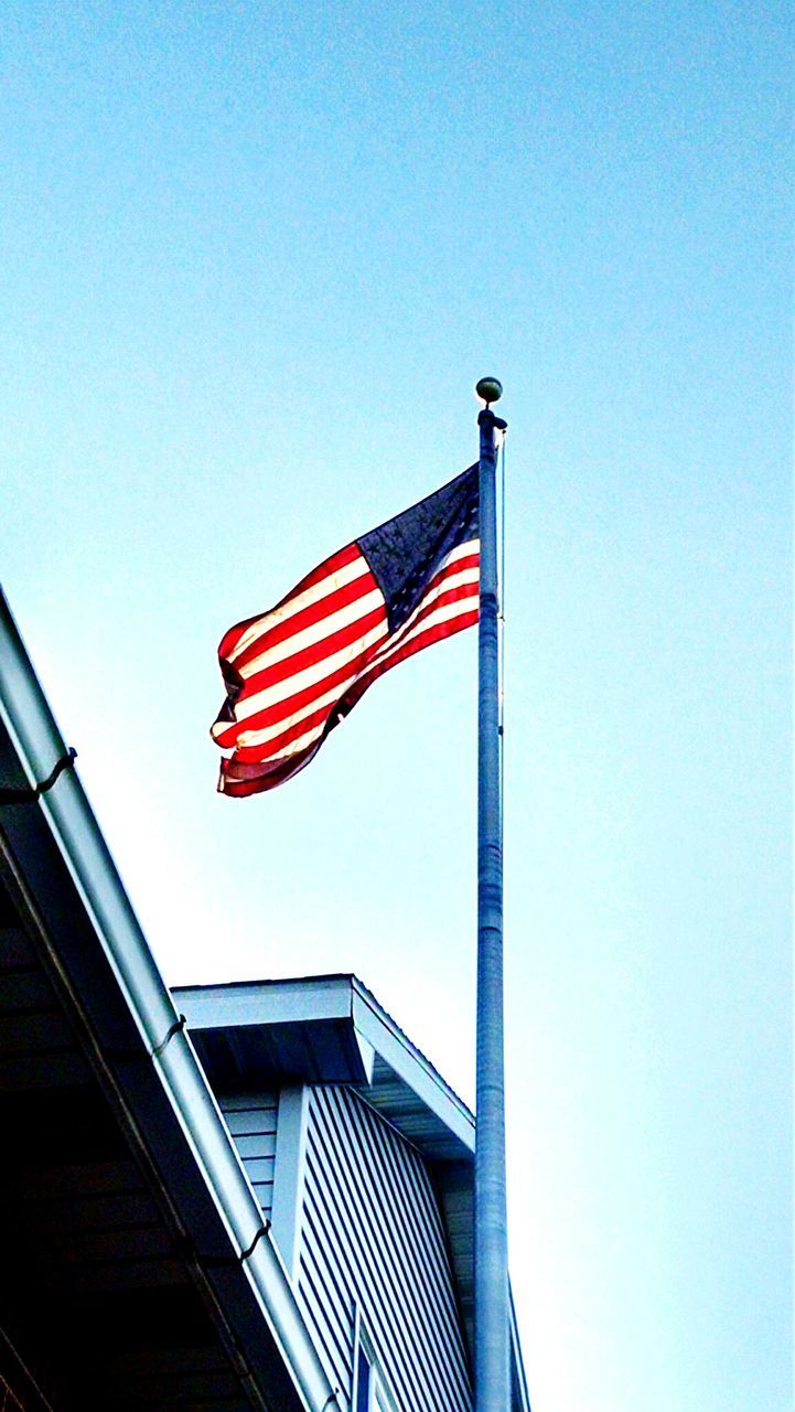 Low angle view of american flag on house roof against clear sky