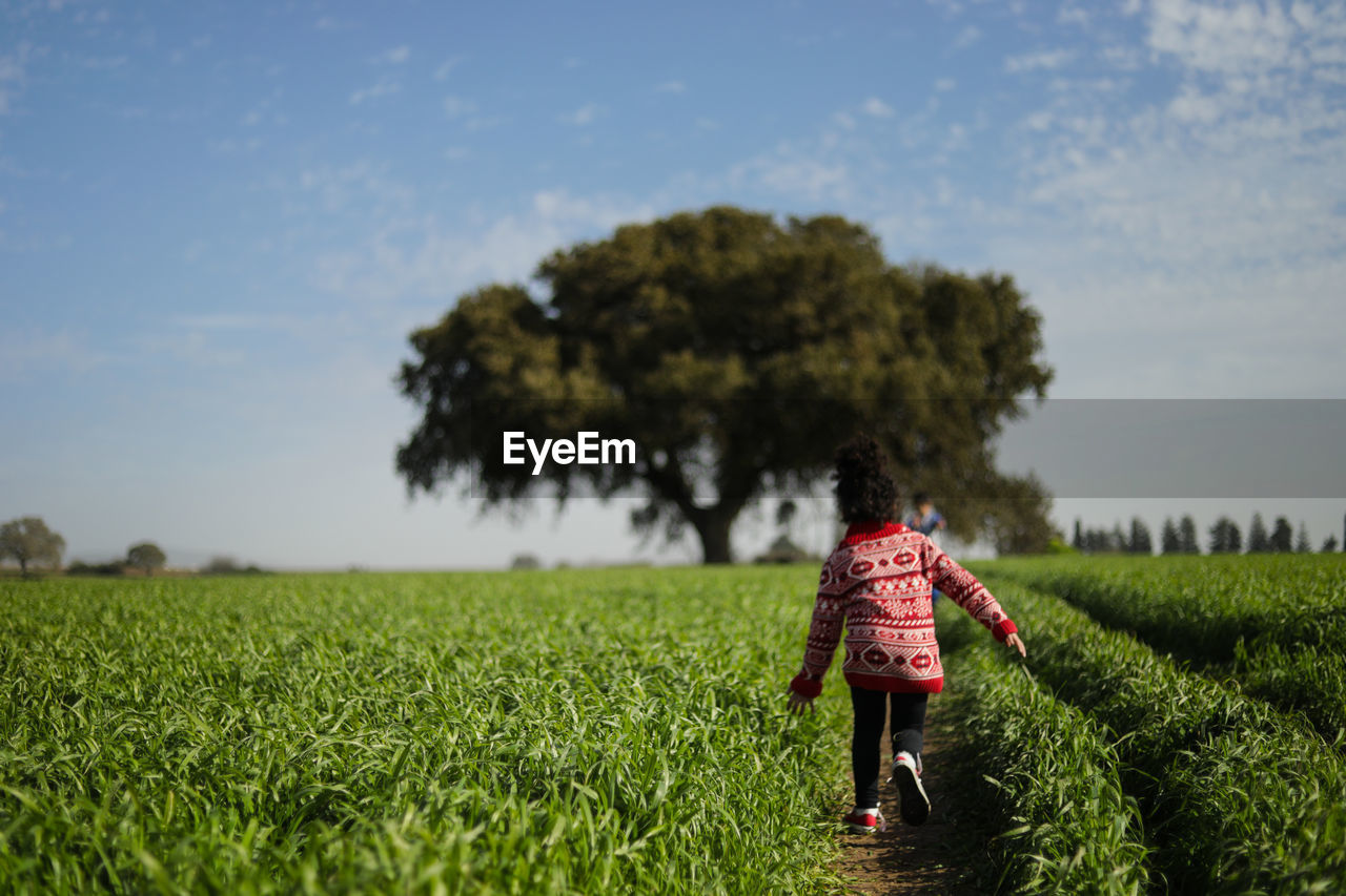 REAR VIEW OF WOMAN STANDING ON FIELD AGAINST TREES