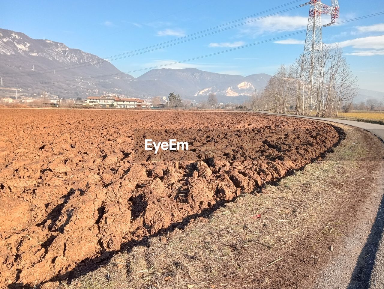 soil, landscape, sky, environment, nature, mountain, land, scenics - nature, field, mountain range, no people, electricity, natural environment, day, road, rural scene, beauty in nature, sunlight, transportation, plant, agriculture, dirt, valley, technology, tranquil scene, electricity pylon, tree, cable, blue, outdoors, tranquility, non-urban scene, desert, rural area, plateau, cloud, power generation