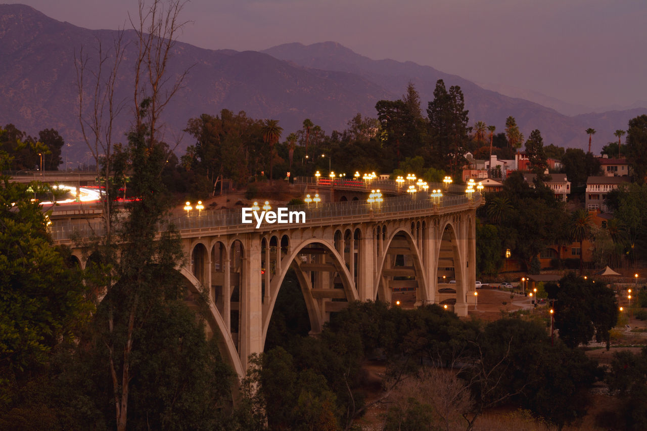 Bridge over illuminated city against sky at dusk