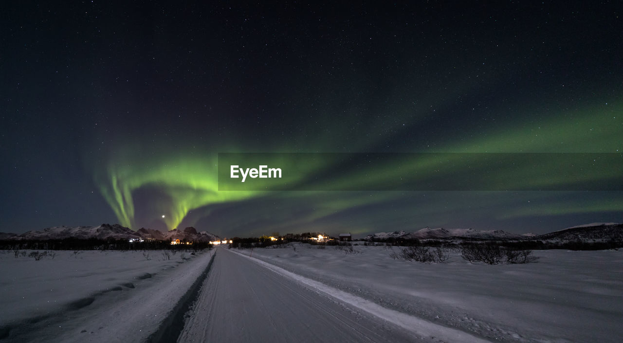 Empty snow covered road against aurora borealis at night