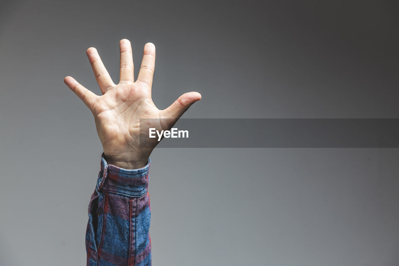 Cropped hand of person gesturing against gray background