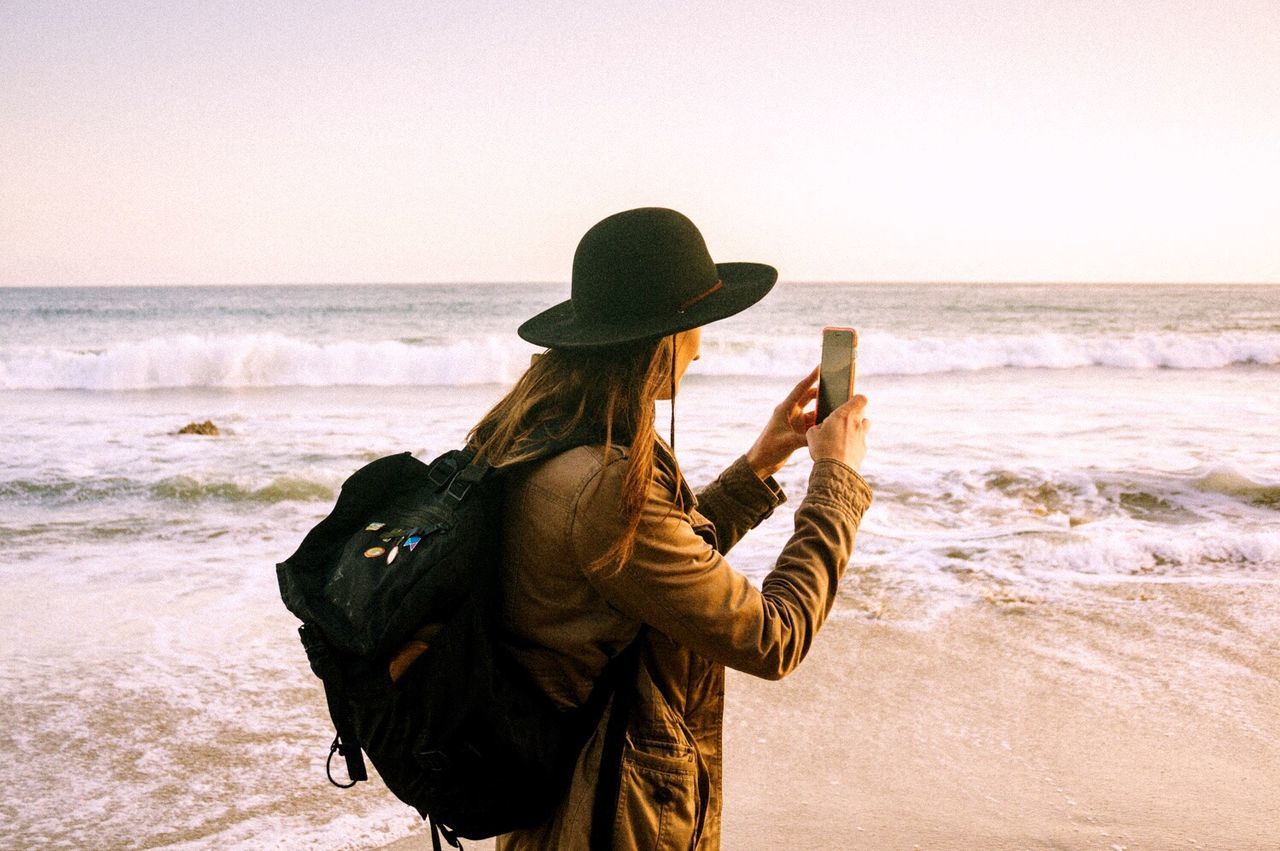Woman photographing sea on beach against clear sky