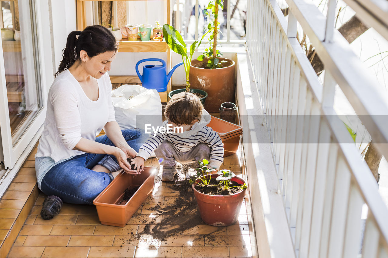 Mother and son planting seed in pot while sitting at balcony