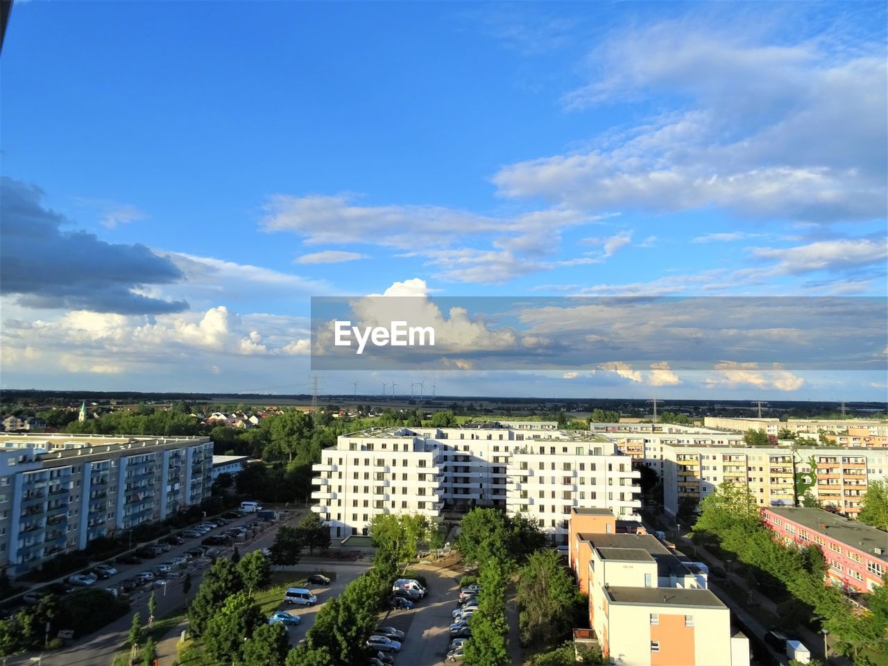 HIGH ANGLE VIEW OF BUILDINGS AND TREES AGAINST BLUE SKY