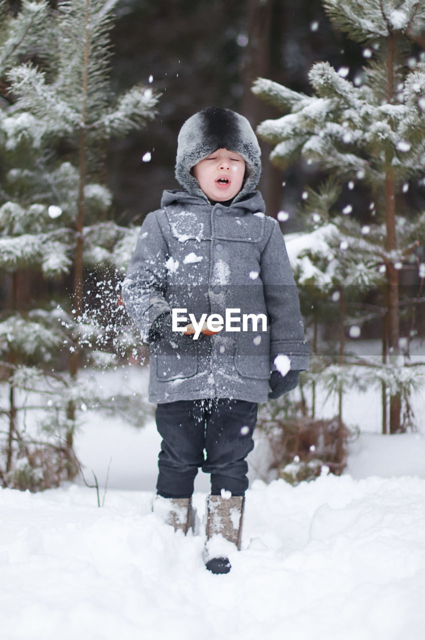 portrait of smiling boy standing on snow covered field during winter