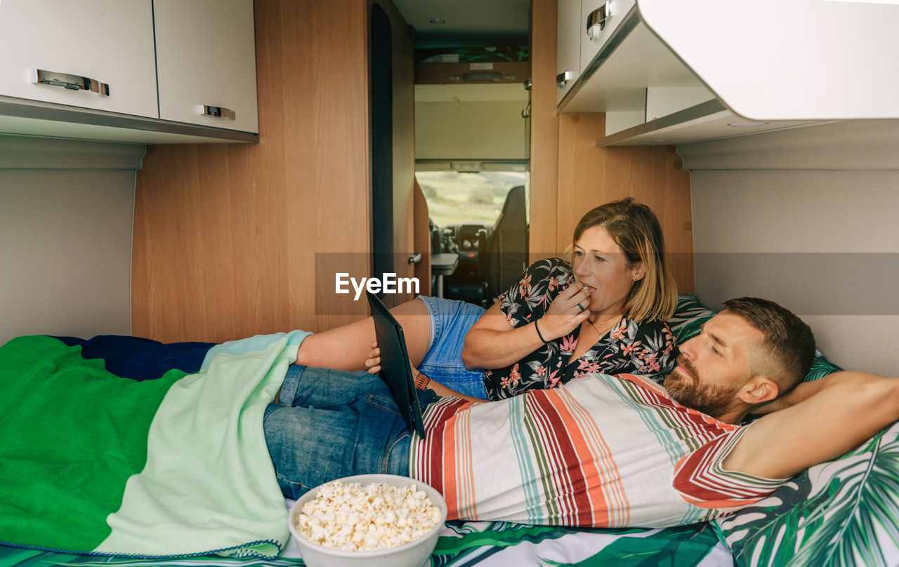 Couple watching a movie lying on the bed of their camper van