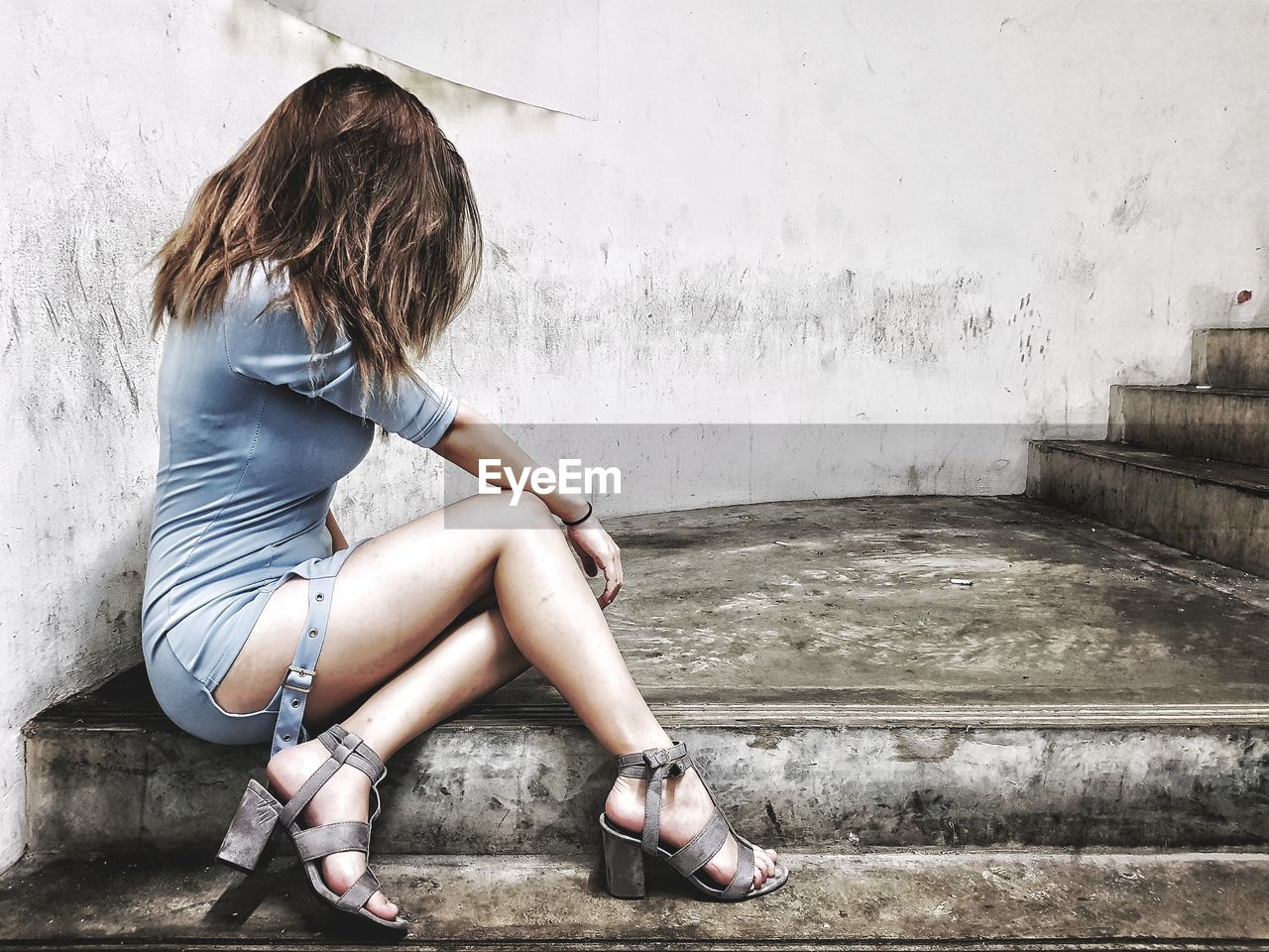 Woman sitting on staircase against wall