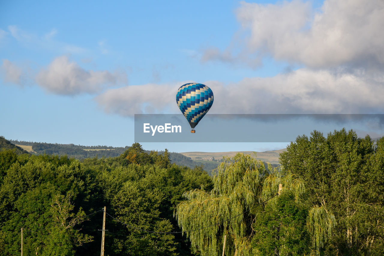 Hot air balloon flying over trees against sky in murol village.