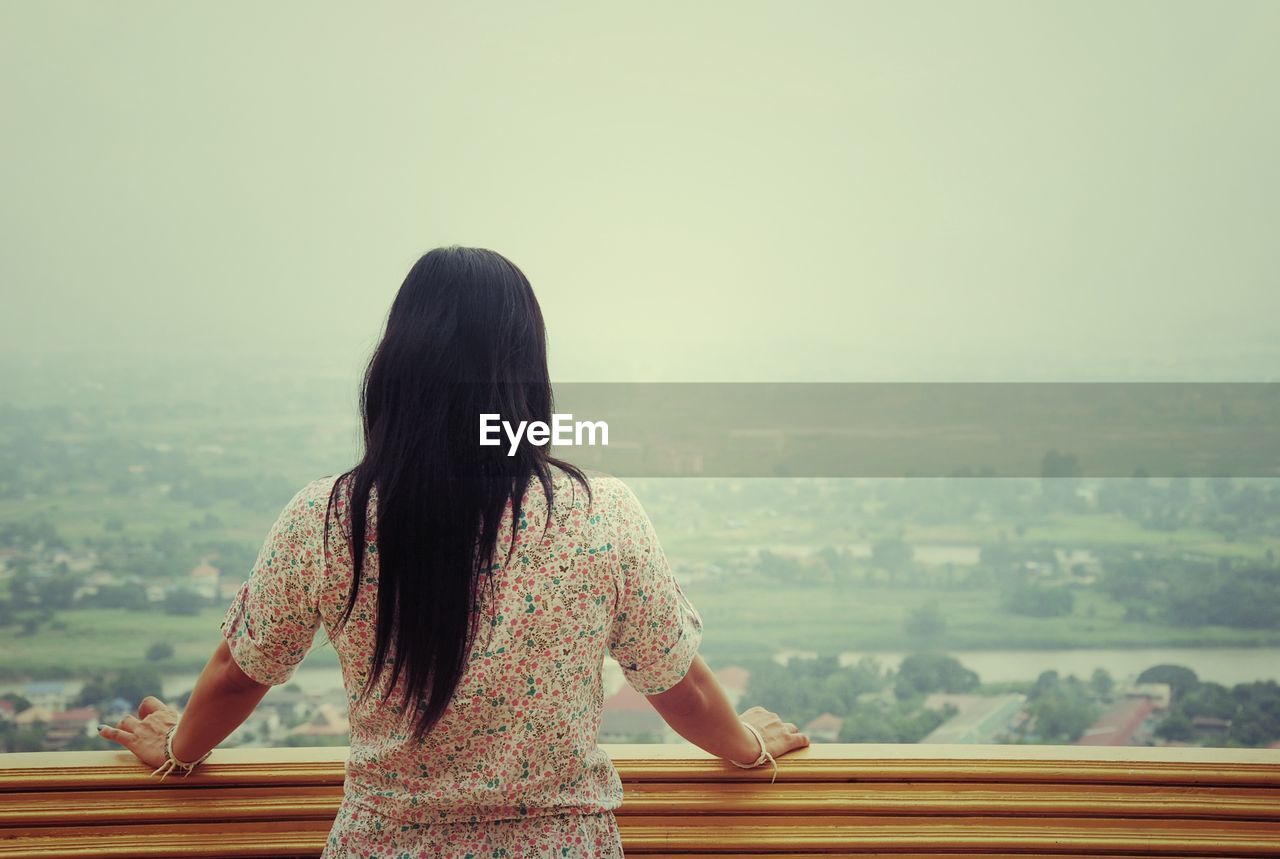 Rear view of woman looking at cityscape against sky