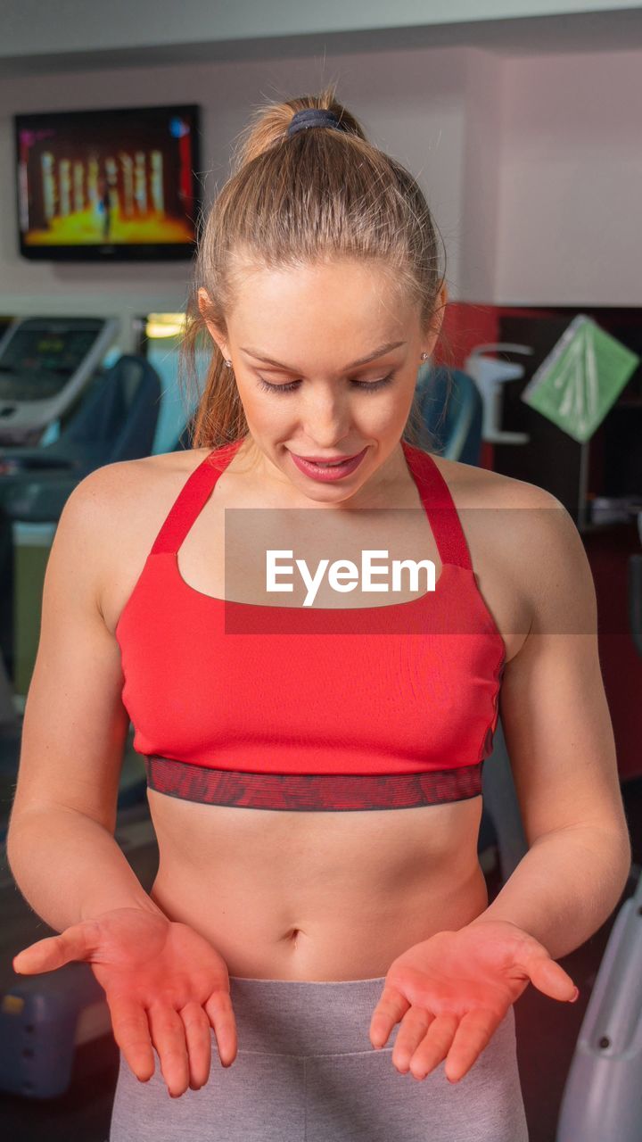 women, adult, one person, lifestyles, exercising, indoors, sports, female, human leg, wellbeing, limb, clothing, smiling, person, standing, young adult, sports clothing, emotion, front view, happiness, looking down, blond hair, sport venue, waist up, arm, physical fitness, looking, child, human hair, gym, positive emotion, healthcare and medicine, anticipation