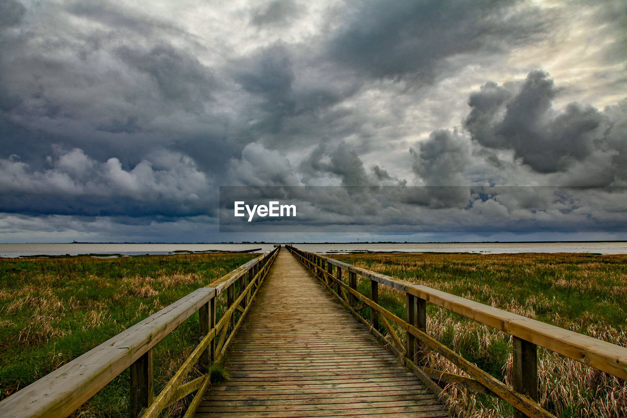 Wooden boardwalk on field against sky