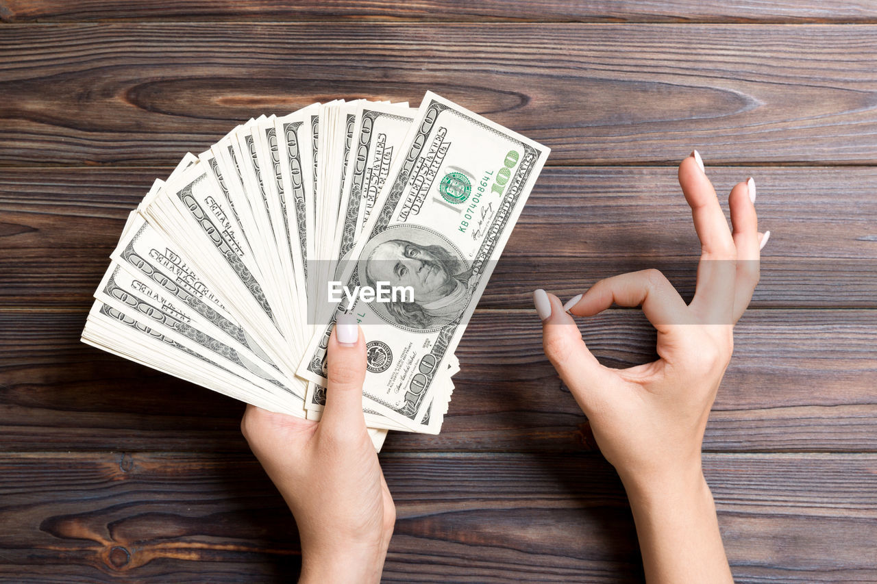 Directly above shot of woman hand gesturing while holding paper currency on wooden table