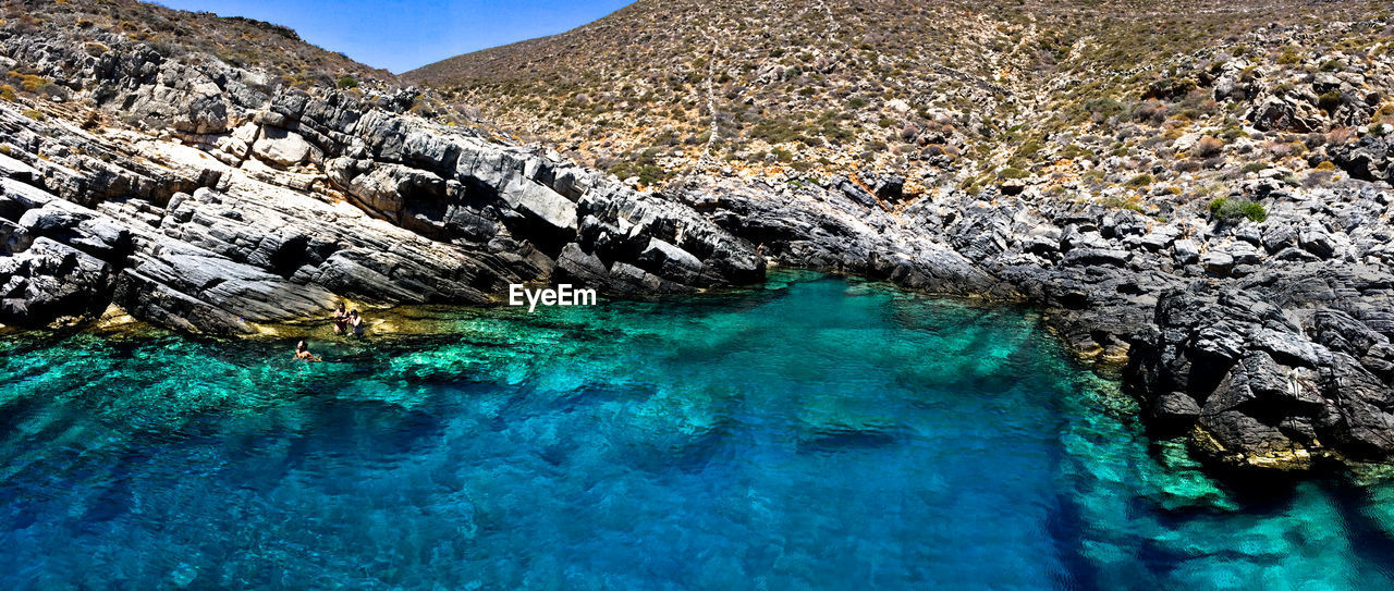 Aerial view of sea by mountain against blue sky