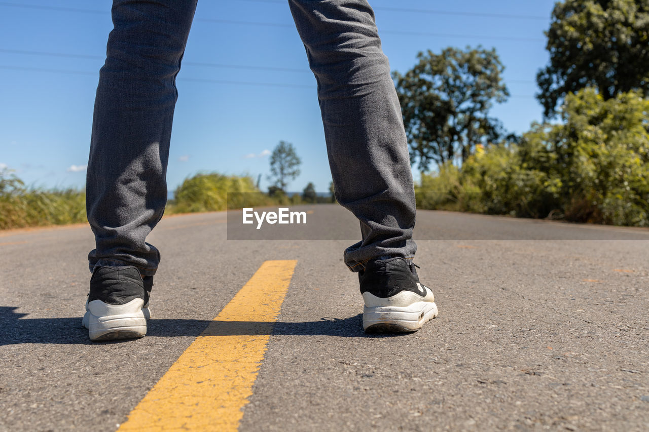 LOW SECTION OF MAN SKATEBOARDING ON ROAD AGAINST SKY