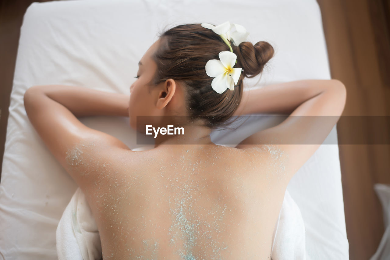 Rear view of shirtless young woman lying on massage table in spa