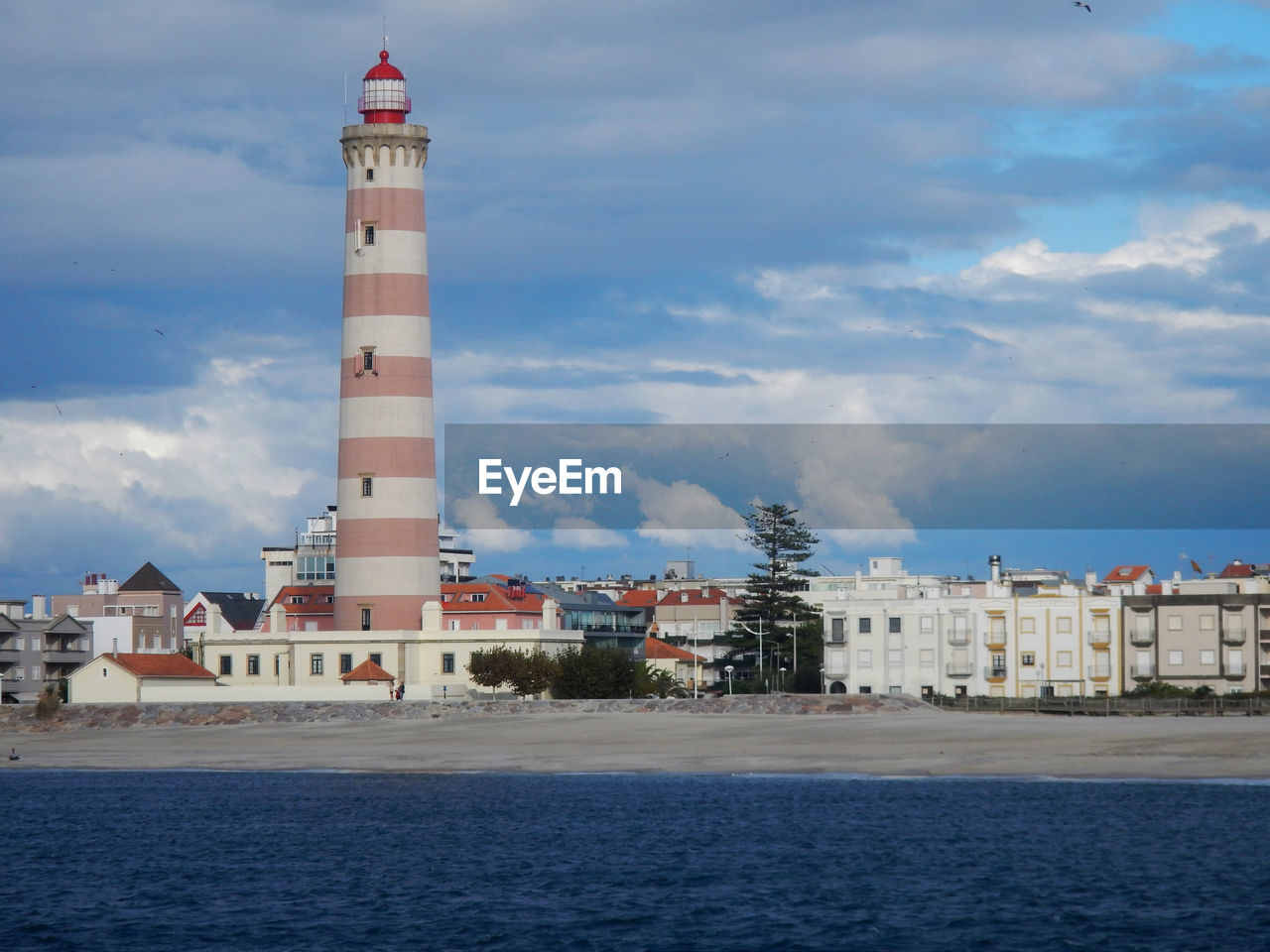 LIGHTHOUSE BY BUILDINGS AGAINST SKY