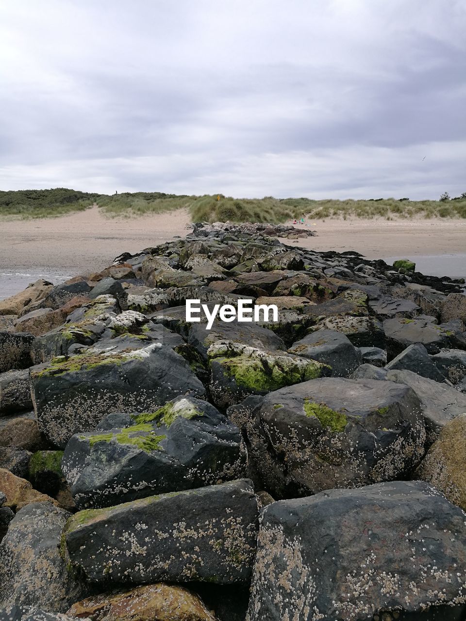 Rock groyne at seashore against cloudy sky